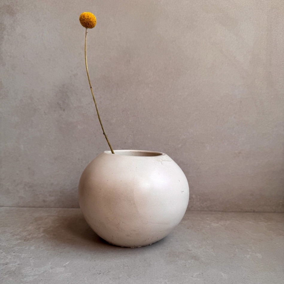 A white round vase with a yellow flower in it Description automatically generated