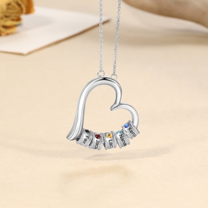 May include: A silver heart-shaped necklace with six small rings attached to the bottom. Each ring has a different colored gemstone and a name engraved on it: Fair, Jack, Lac, Nana, Xeni.