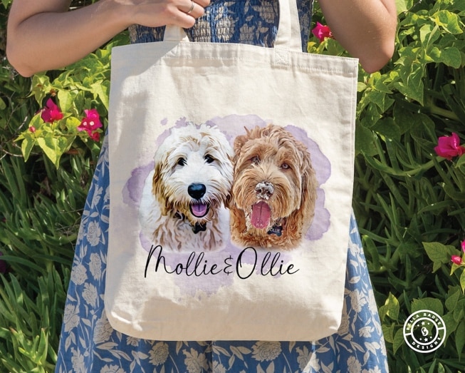 May include: A white canvas tote bag with a watercolor design of two dogs. The dogs are a white and brown doodle and a brown doodle. The text on the bag reads 'Mollie & Ollie'.