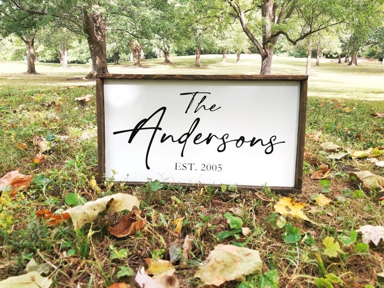 May include: A white wooden sign with a brown frame. The sign says 'The Andersons EST. 2005' in black cursive font.