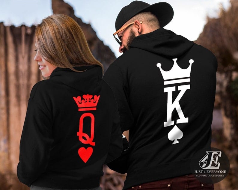 May include: Two black hoodies with white and red designs. The hoodie on the left has a red queen of hearts design with a crown on top. The hoodie on the right has a white king of spades design with a crown on top. The text 'JUST 4 EVERYONE CLOTHING ACCESSORIES' is visible on the bottom right corner of the image.