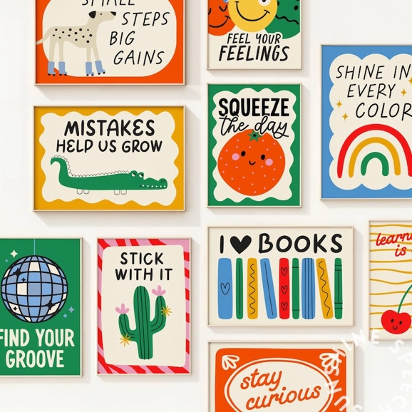 May include: A collection of framed art prints with colorful illustrations and motivational phrases. The prints feature a variety of designs, including a dog, a crocodile, a disco ball, a cactus, a rainbow, and a smiling orange. Text includes "Small Steps Big Gains" and "I Love Books."