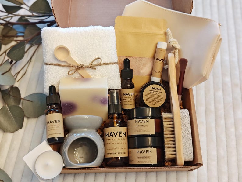 May include: A gift box filled with self-care items. Includes a white washcloth, wooden spoon, soap, essential oils, lip balm, a ceramic oil diffuser, and other spa products. The products are from Haven.