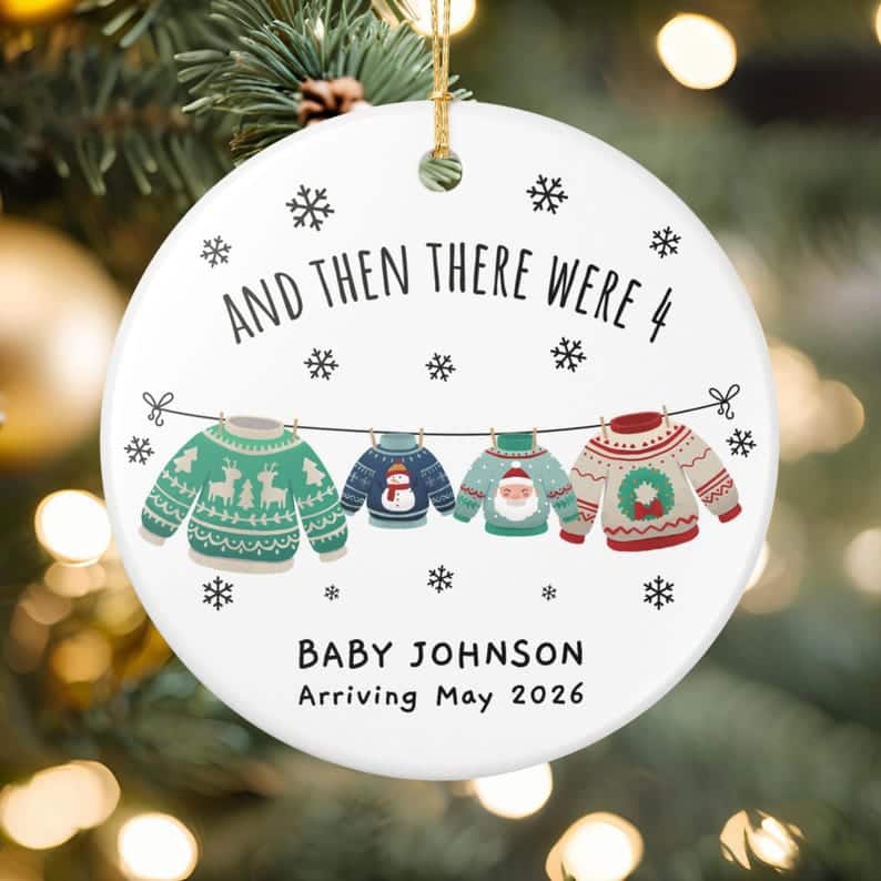 May include: A white ceramic Christmas ornament with the text "AND THEN THERE WERE 4" and "BABY JOHNSON Arriving May 2026". The ornament features four sweaters hanging on a clothesline, with snowflake accents.