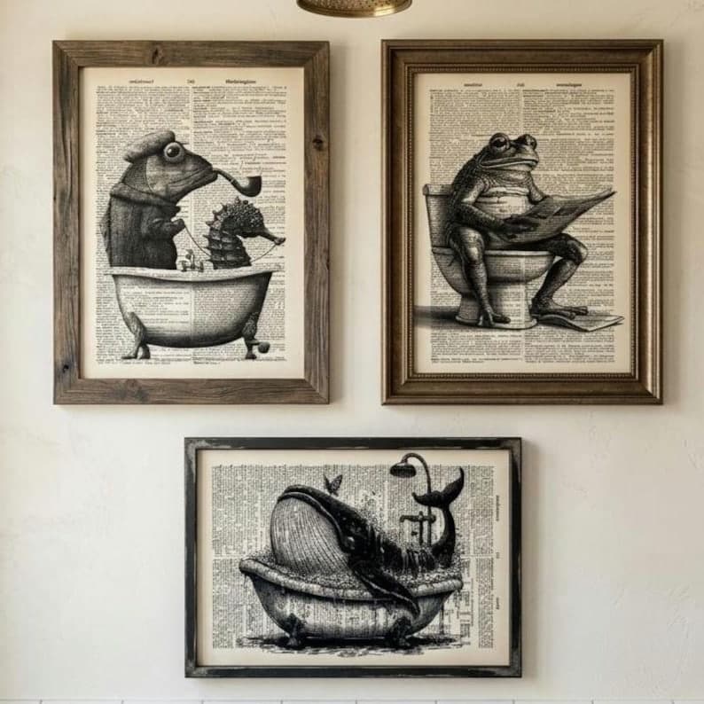 May include: Three framed art prints featuring whimsical illustrations. One shows a frog in a bathtub with a seahorse, another a frog on a toilet reading, and the last a whale in a bathtub with a shower.