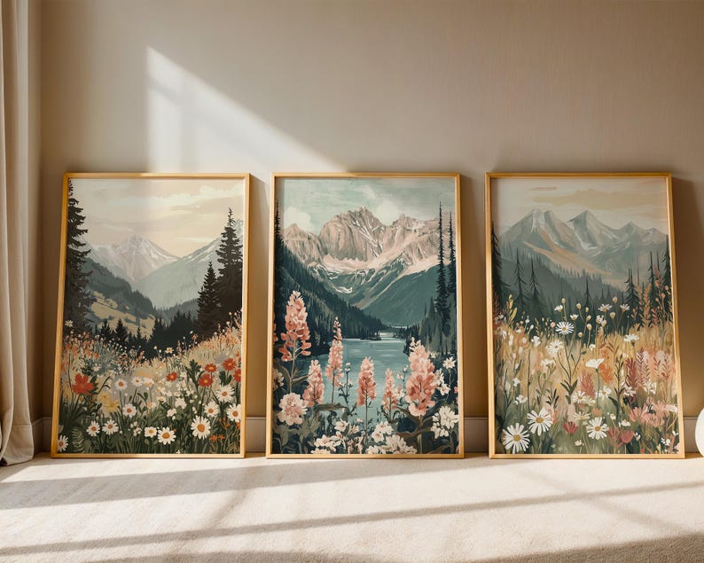 May include: Three framed landscape art prints. Each print features a mountain scene with wildflowers in the foreground. The color palette includes greens, blues, and earth tones. The frames are a light gold color.